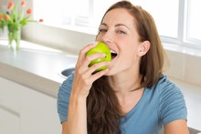 Smiling Young Woman Eating Apple In Kitchen