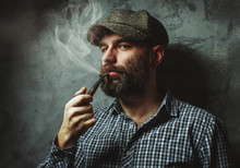 Man Smokes A Pipe Standing Near The Wall