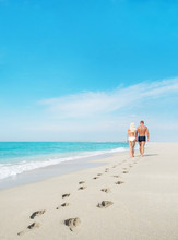Loving Couple Walking With Footprints At Sea Sandy Beach