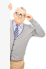 Wall Mural - Senior gentleman with glasses standing behind a blank panel