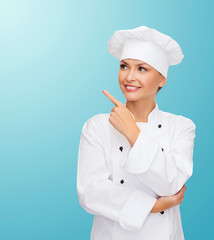 Canvas Print - smiling female chef pointing finger to sonething