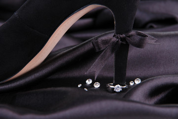 Beautiful ring on heel of black female shoe, on silk background