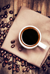 Poster - Cup of coffee with coffee beans on  brown napkin on wooden table