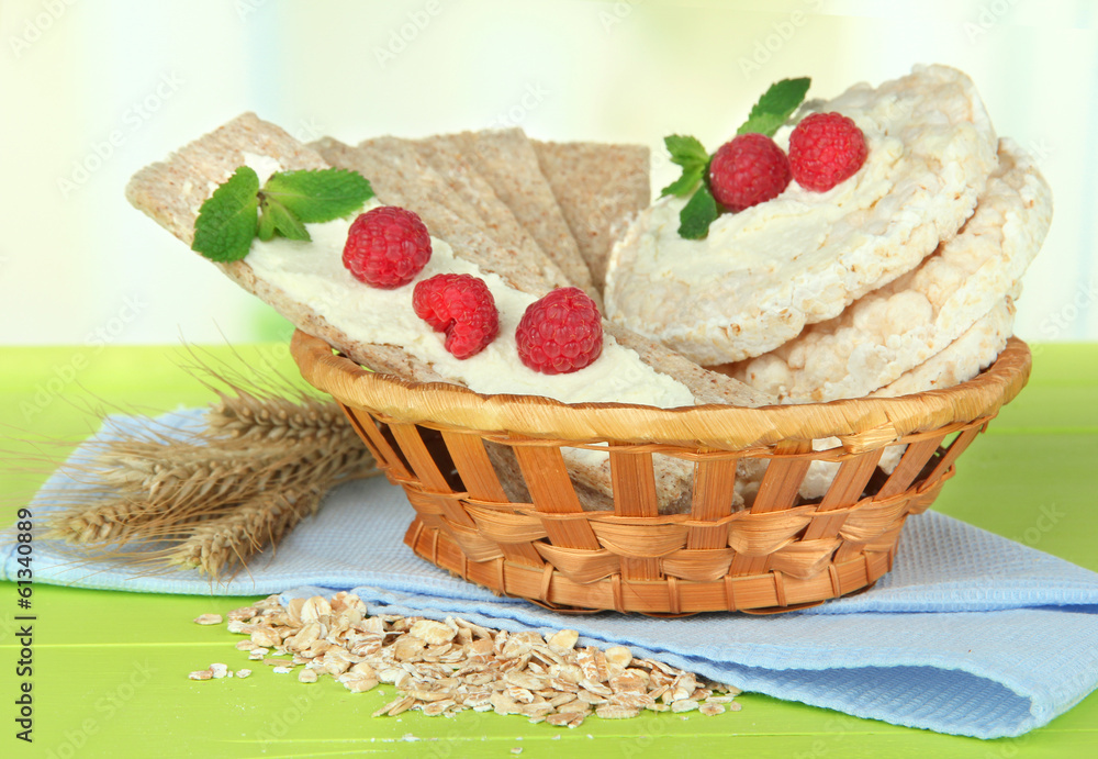 Tasty crispbread with berries in wicker basket, on green table