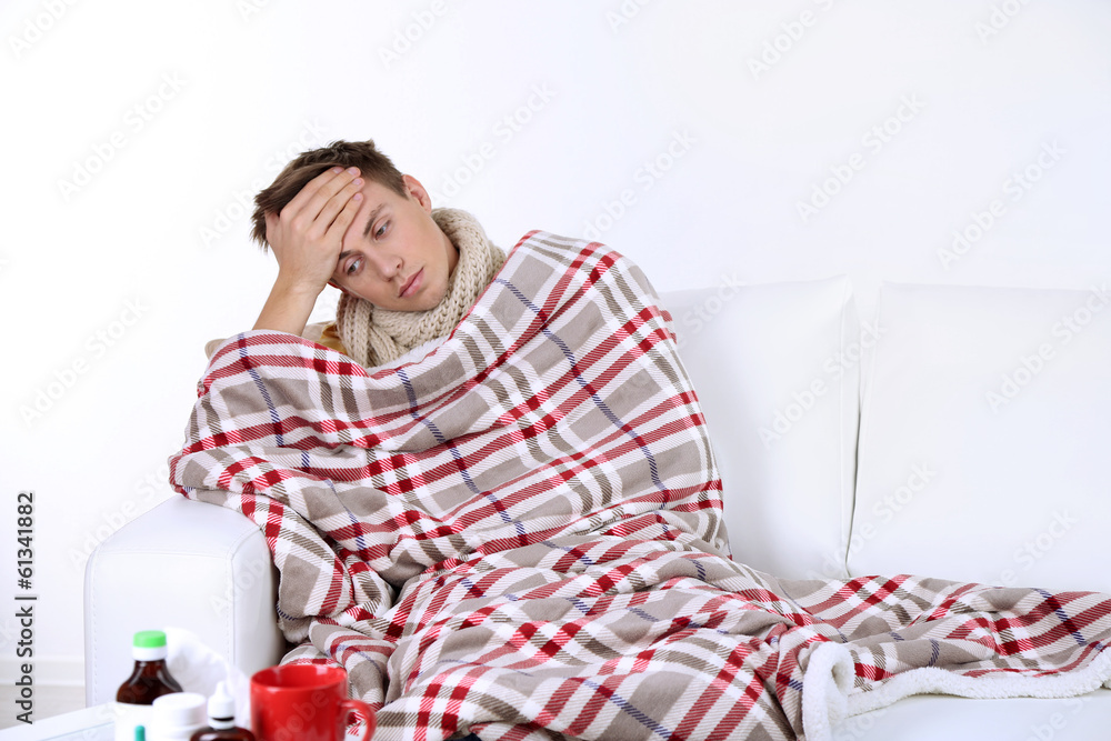 Guy wrapped in plaid sitting on sofa is ill