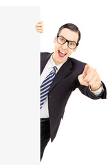 Sticker - Smiling young businessman pointing with finger behind blank pane