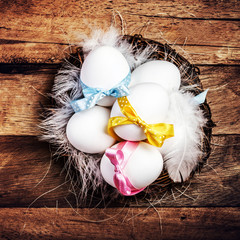 Easter nest with Eggs,  ribbons and white feathers on wooden bac