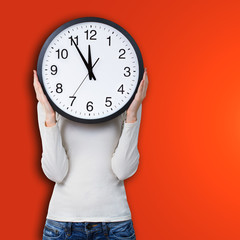 Woman holding a clock over face against orange background