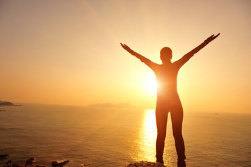 Sticker - cheering woman open arms to sunrise at seaside mountain rock