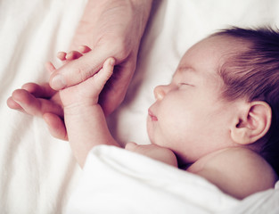 newborn baby and his father's hand - care and safety concept