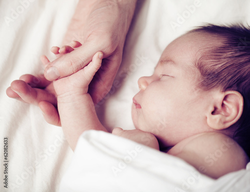 Fotografie, Obraz Newborn baby and his father's hand - care and safety concept