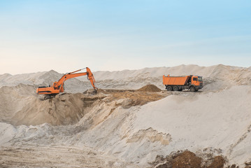 Track excavator loading soil on truck in front of a cloudy sky