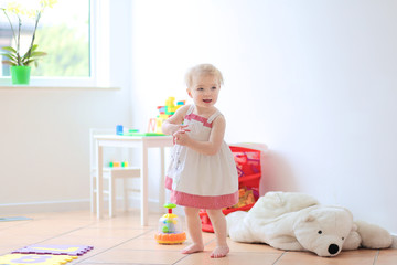 Wall Mural - Happy blonde toddler girl having fun dancing indoors