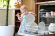 toddler girl helping in kitchen taking plates out of dish washer