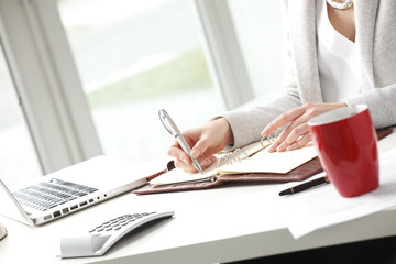 Businesswoman sitting at desk and makes a note in office.