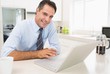 © WavebreakMediaMicro - Smiling well dressed man using laptop in kitchen