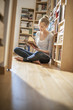 © jackfrog - young woman sit on the floor reads a book near home library