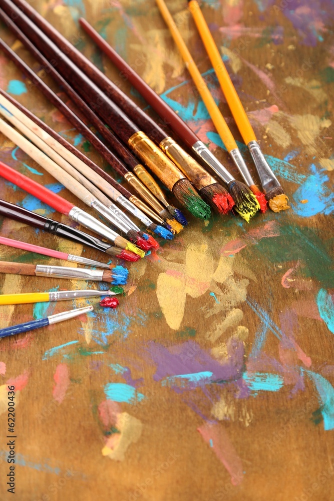 Many brushes in paints on multicolor wooden background