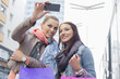 © MDBPIXS - Female friends with shopping bags taking photos through mobile phone