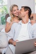 © lightwavemedia - Happy casual couple using laptop in living room