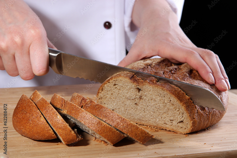 Cutting bread on wooden board on dark background