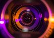 Video camera lens closeup lit by orange and purple neon light