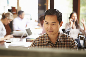 Canvas Print - Businessman Working At Desk With Meeting In Background