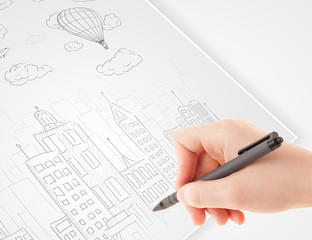 Fototapete - A person drawing sketch of a city with balloons and clouds on a