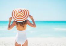 Young Woman In Hat Standing On Beach. Rear View