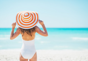 Wall Mural - Young woman in hat standing on beach. rear view