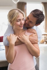 Wall Mural - Man embracing woman from behind at home