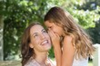 © lightwavemedia - Girl whispering secret into mother's ear at park