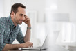 © Mint Images - Office Interior. A Man Seated At A Table, Using A Laptop Computer.