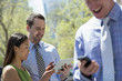 © Mint Images - A Businesswoman And Two Businessmen Outdoors In The City. Checking Their Phones.