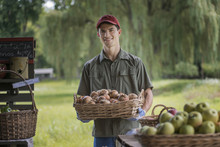 Organic Farmer, Young Man Holding Baskets Of Fresh Fruit At A Market Farm Stand. 