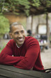 © Mint Images - Scenes from urban life in New York City. A man in a red jumper seated at a bench, smiling.