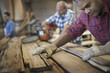 © Mint Images - A reclaimed lumber workshop. A group of people working. A man measuring and checking planks of wood for re-use and recycling.