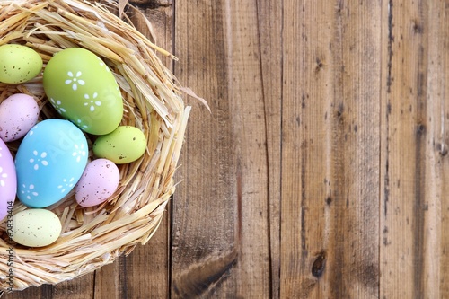 Easter eggs in nest on color wooden background Poster