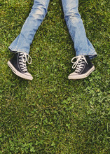 A Ten Year Old Girl Lying On The Grass. Cropped View Of Her Lower Legs. Wearing Sneakers And Faded Blue Jeans. 