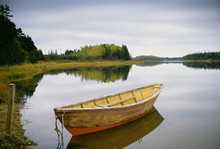 A small wooden dory or rowing boat moored on flat calm water, in Savage harbour on Prince Edward Island in Canada.