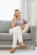 © Alliance - Happy young woman sitting on divan and talking cell phone