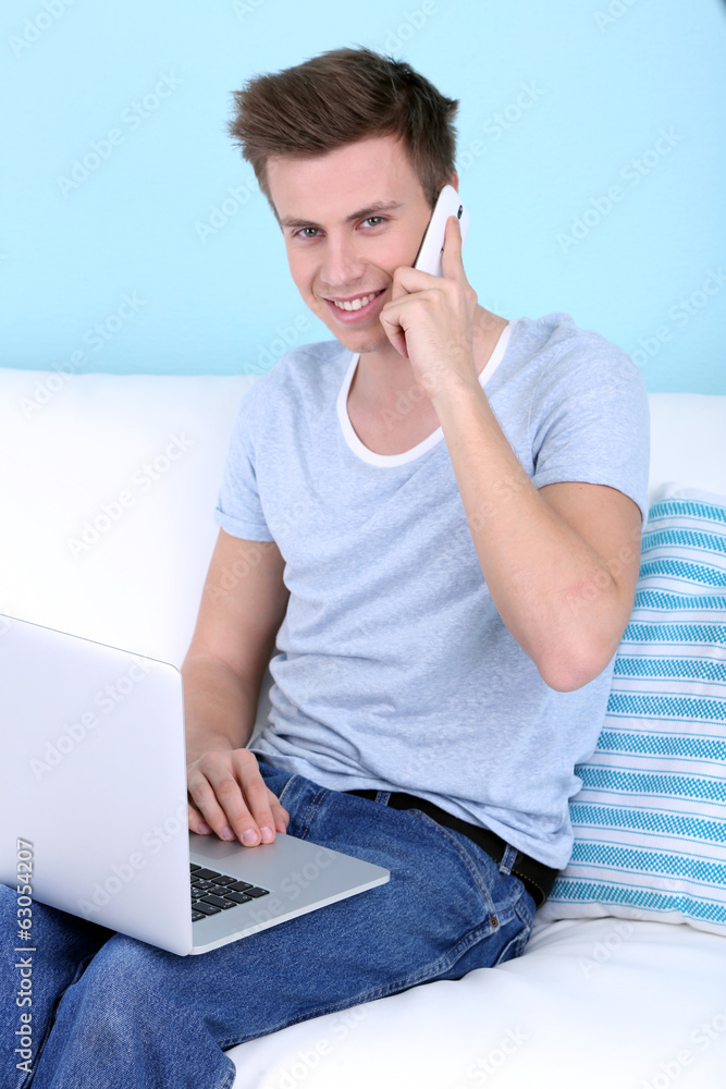 Guy talking of phone with laptop on blue background