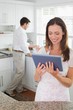 © lightwavemedia - Woman using digital tablet with man in background in kitchen