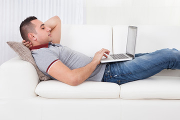 Man Using Laptop While Lying On Sofa