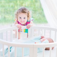 Wall Mural - Cute toddler girl playing with her newborn baby brother in a bed