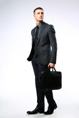 Wall Mural - Confident businessman with bag looking away over gray background