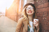 Fototapeta  - Cheerful woman in the street drinking morning coffee in sunshine