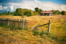 Old House With Wooden Fence On The Empty Meadow