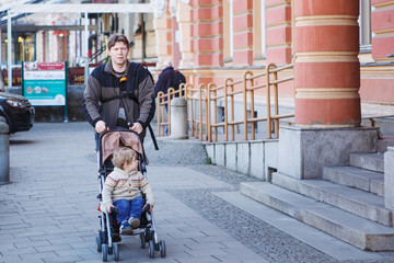 Father walking with little son in stroller in the city