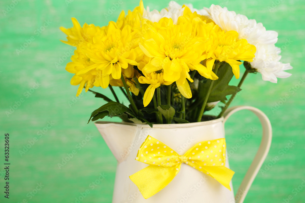 Beautiful chrysanthemum flowers in pitcher on wooden background